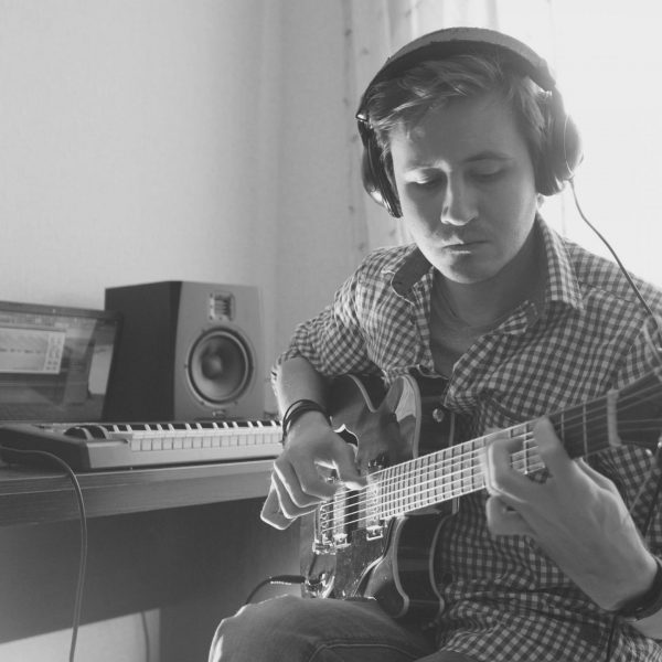 Young musician composes and records music playing the guitar, using computer, from the front view
